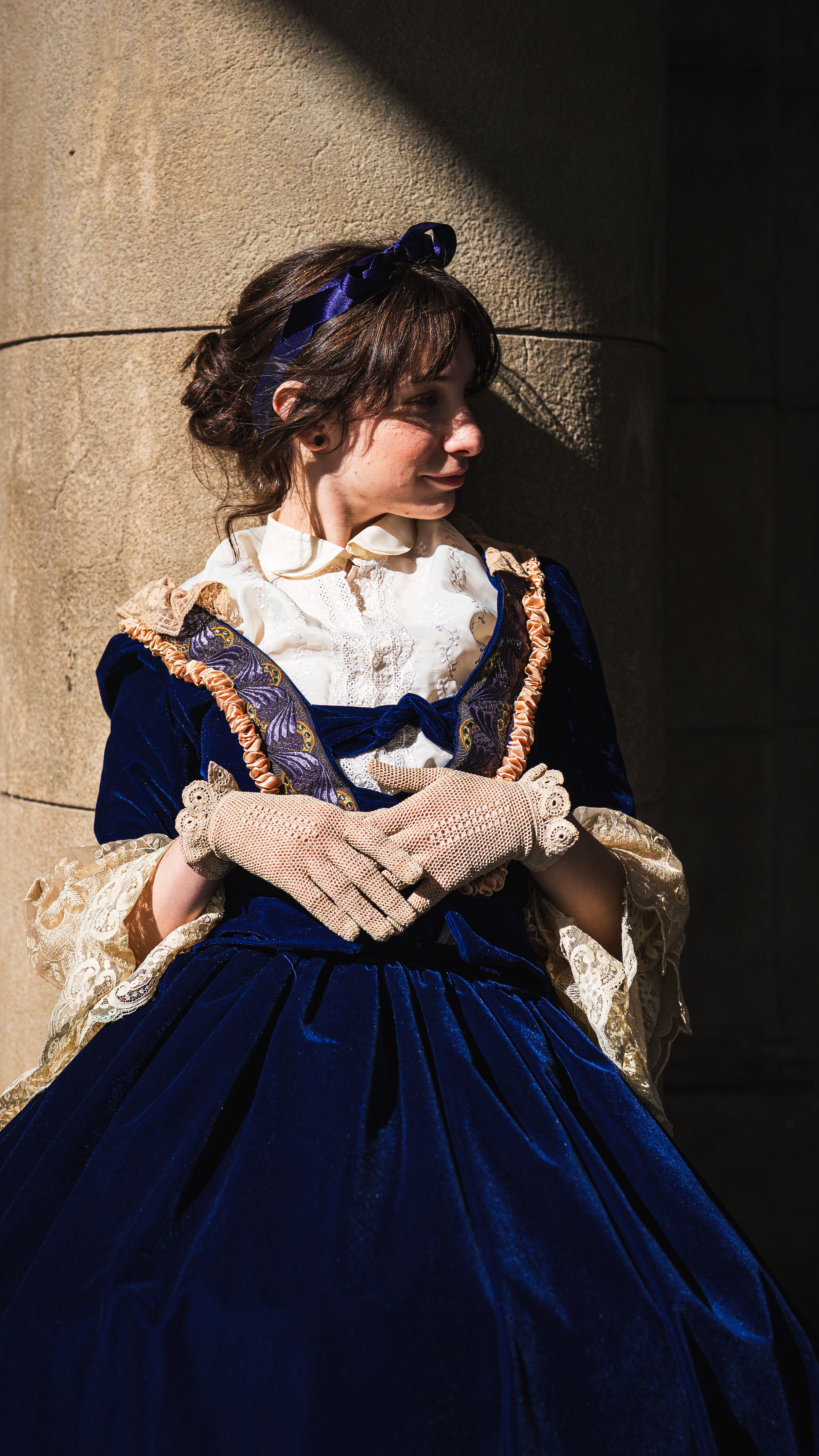 Woman in vintage Victorian attire posing by a stone column.