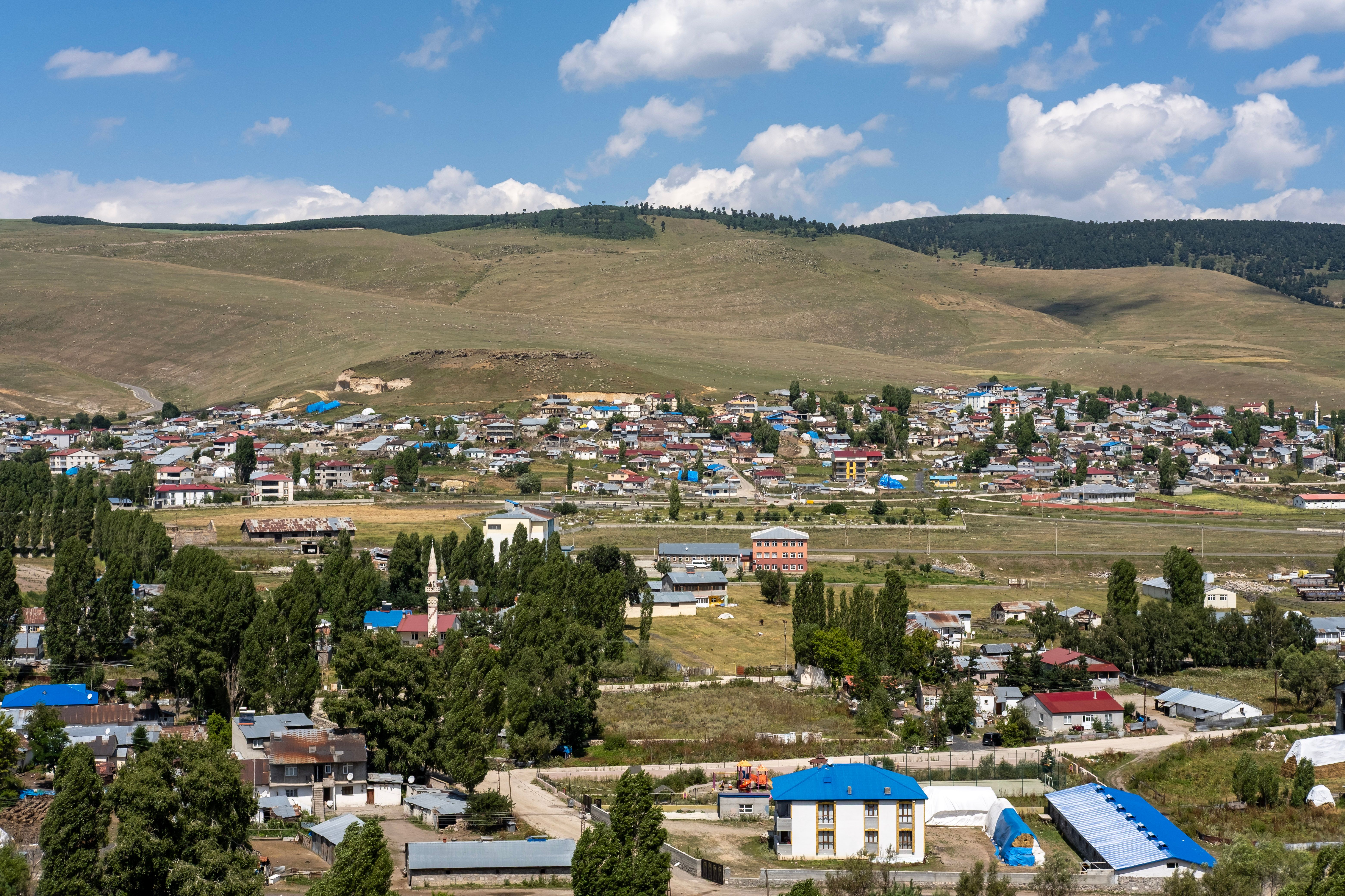 Picturesque aerial view of a small town surrounded by hills and lush greenery under a clear blue sky.