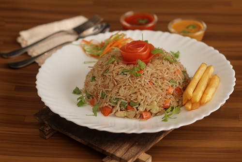 Free Tasty vegetable fried rice with a tomato rose and fries on a wooden background. Stock Photo