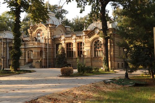 Free A historic building with ornate architecture in a sunlit park setting, surrounded by trees. Stock Photo