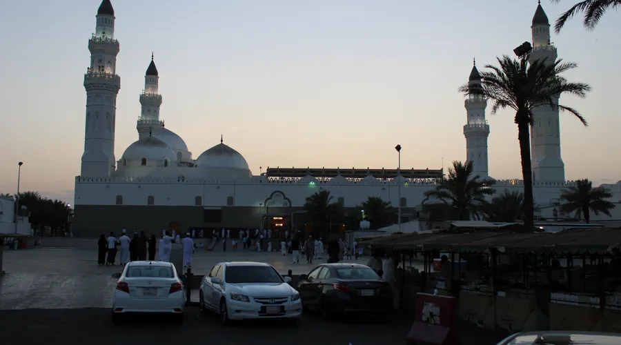 Masjid Quba in Madinah at twilight, with its white minarets and domes and pilgrims outside