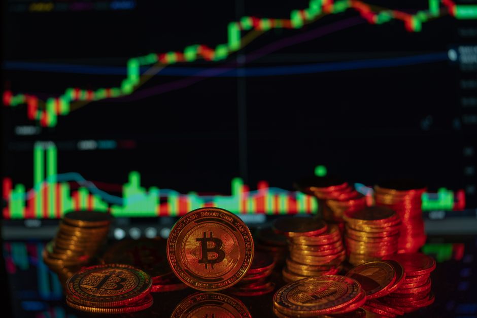 Stacks of Bitcoin coins with a financial market chart in the background, depicting cryptocurrency trading.