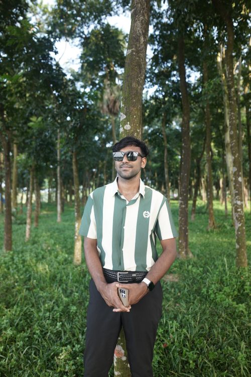 Free Man in striped shirt enjoying a peaceful moment in a lush green forest with sunlight filtering through trees. Stock Photo