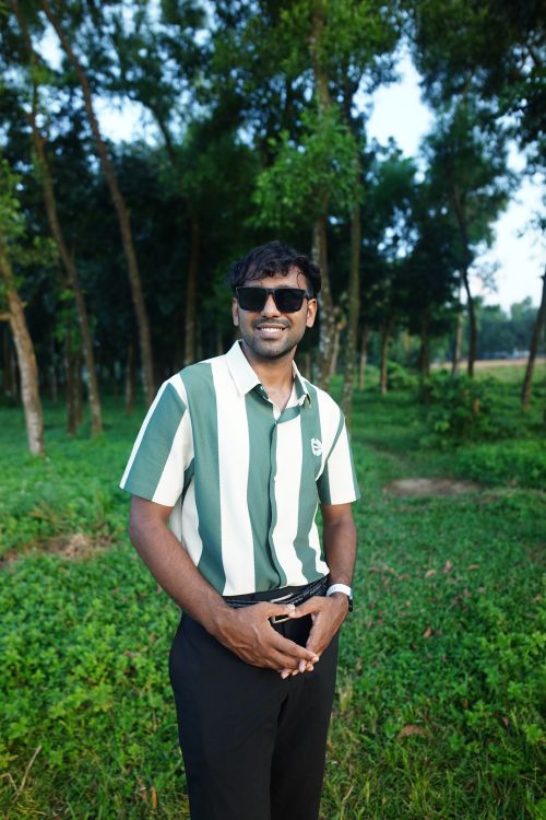 Free Smiling man wearing sunglasses and green striped shirt standing in a lush park. Stock Photo