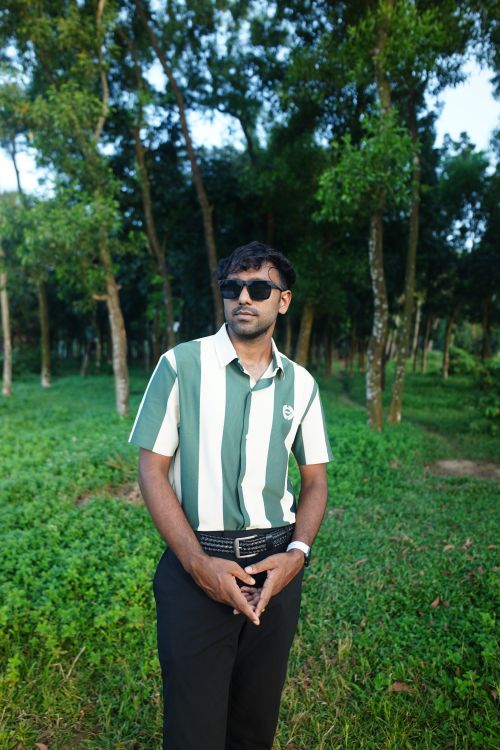 Free Portrait of a stylish man wearing sunglasses and striped shirt posed in a lush green forest. Stock Photo