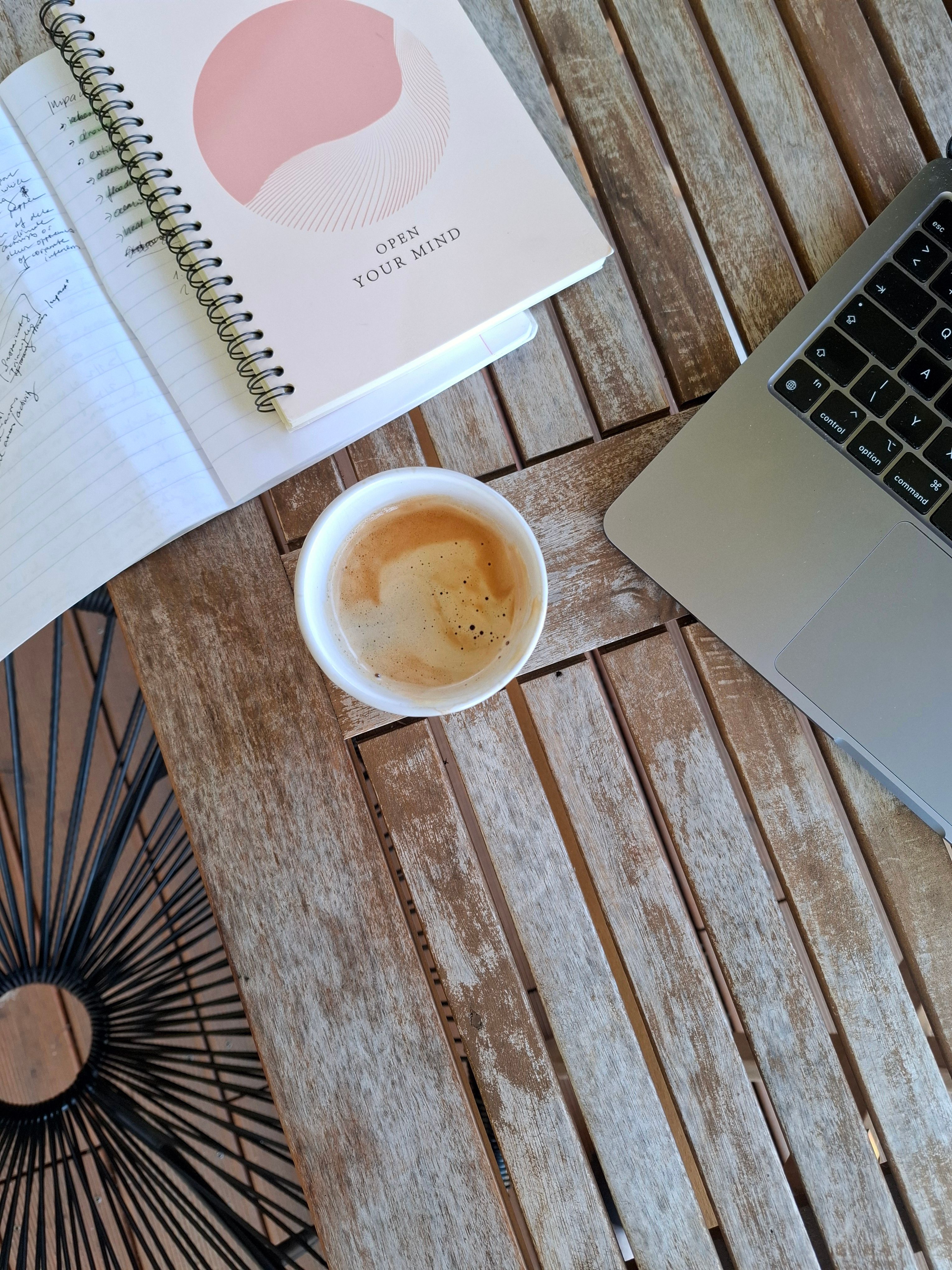 A cozy workspace setup with a laptop, coffee, and open notebook on a rustic wooden table.