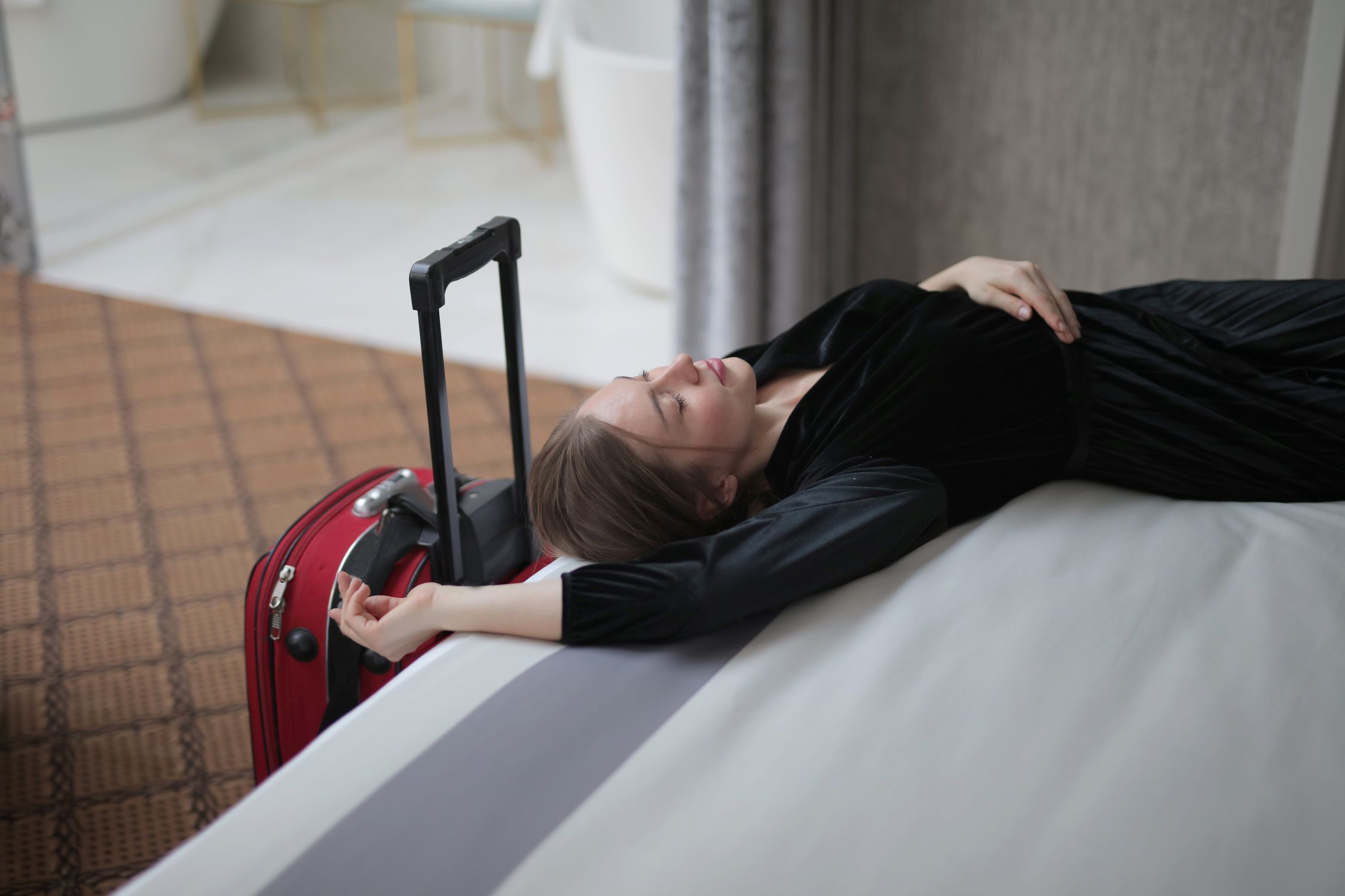 Woman resting on a hotel bed beside her suitcase after a long flight