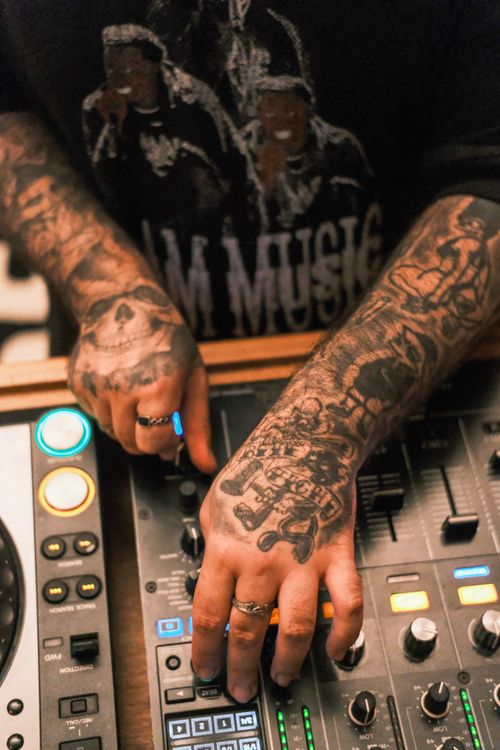 Free Close-up of tattooed hands operating a DJ console in a vibrant setting. Stock Photo
