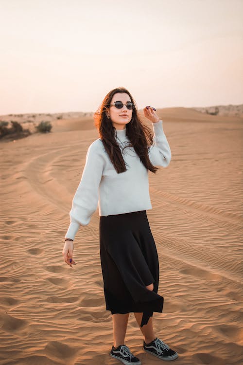 Woman In White Long Sleeve Shirt And Black Skirt Standing On Brown Sand