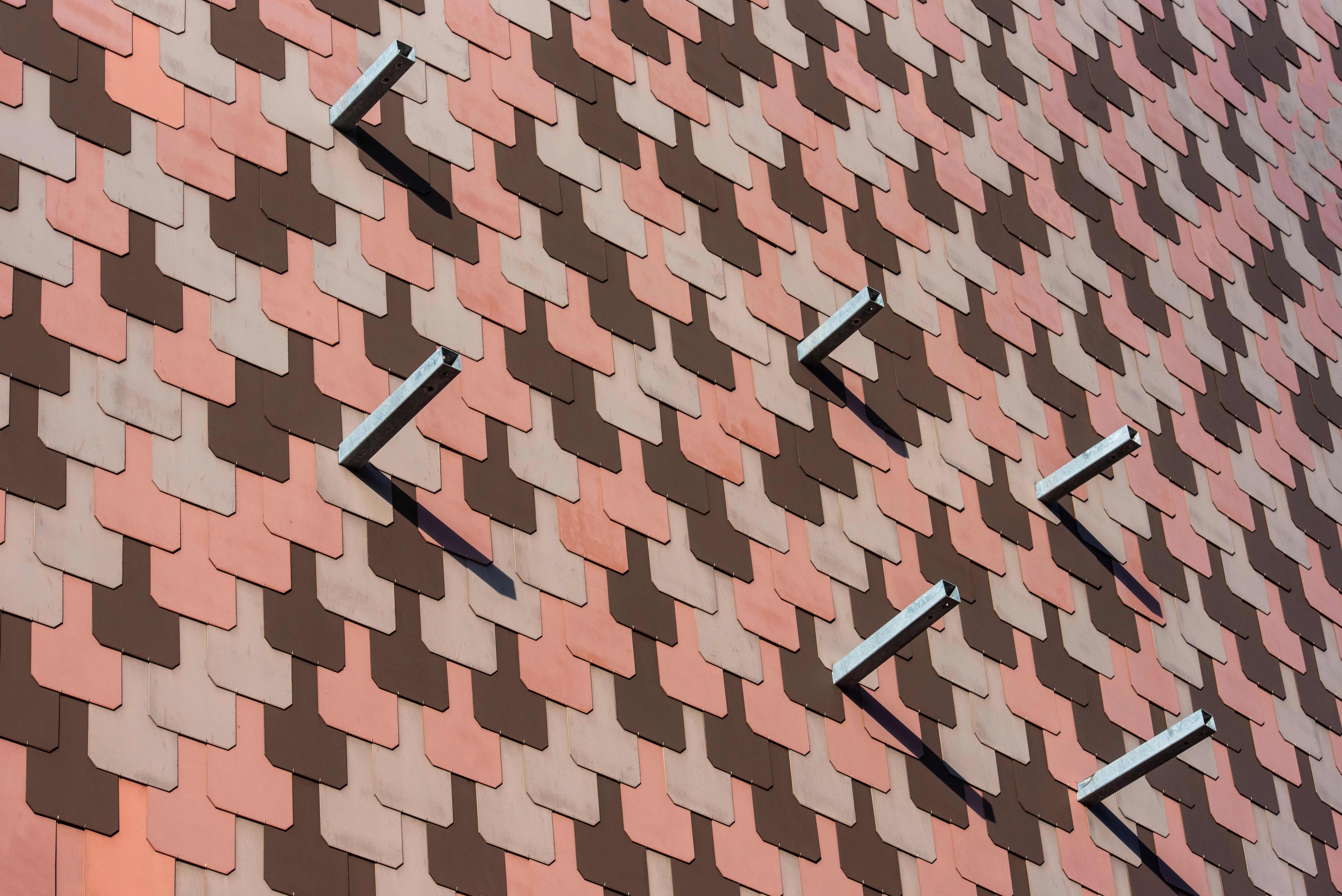 Close-up of a building facade with overlapping red and brown tiles creating a geometric pattern.