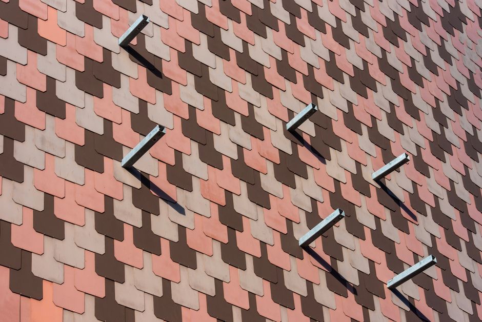 Close-up of a building facade with overlapping red and brown tiles creating a geometric pattern.