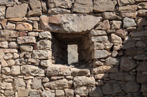 Free A close-up of an ancient stone wall featuring a small window opening. Stock Photo