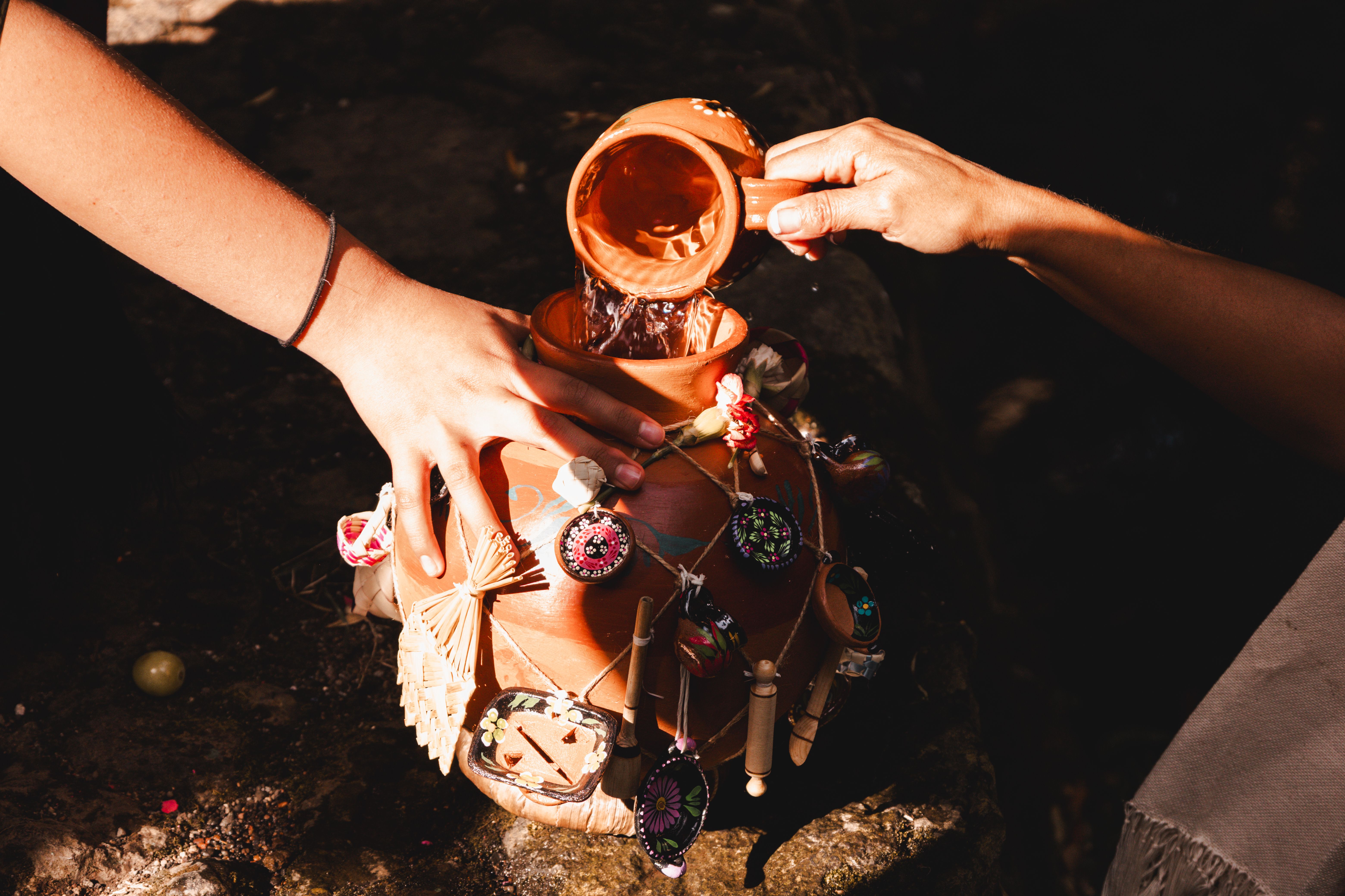 Hands pouring water into a traditional decorated Mexican clay pot during a ceremony in Uruapan, Michoacán, Mexico.