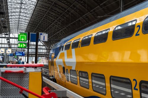 Free Vibrant yellow train at Amsterdam's bustling Central Station, capturing daily commuter life. Stock Photo