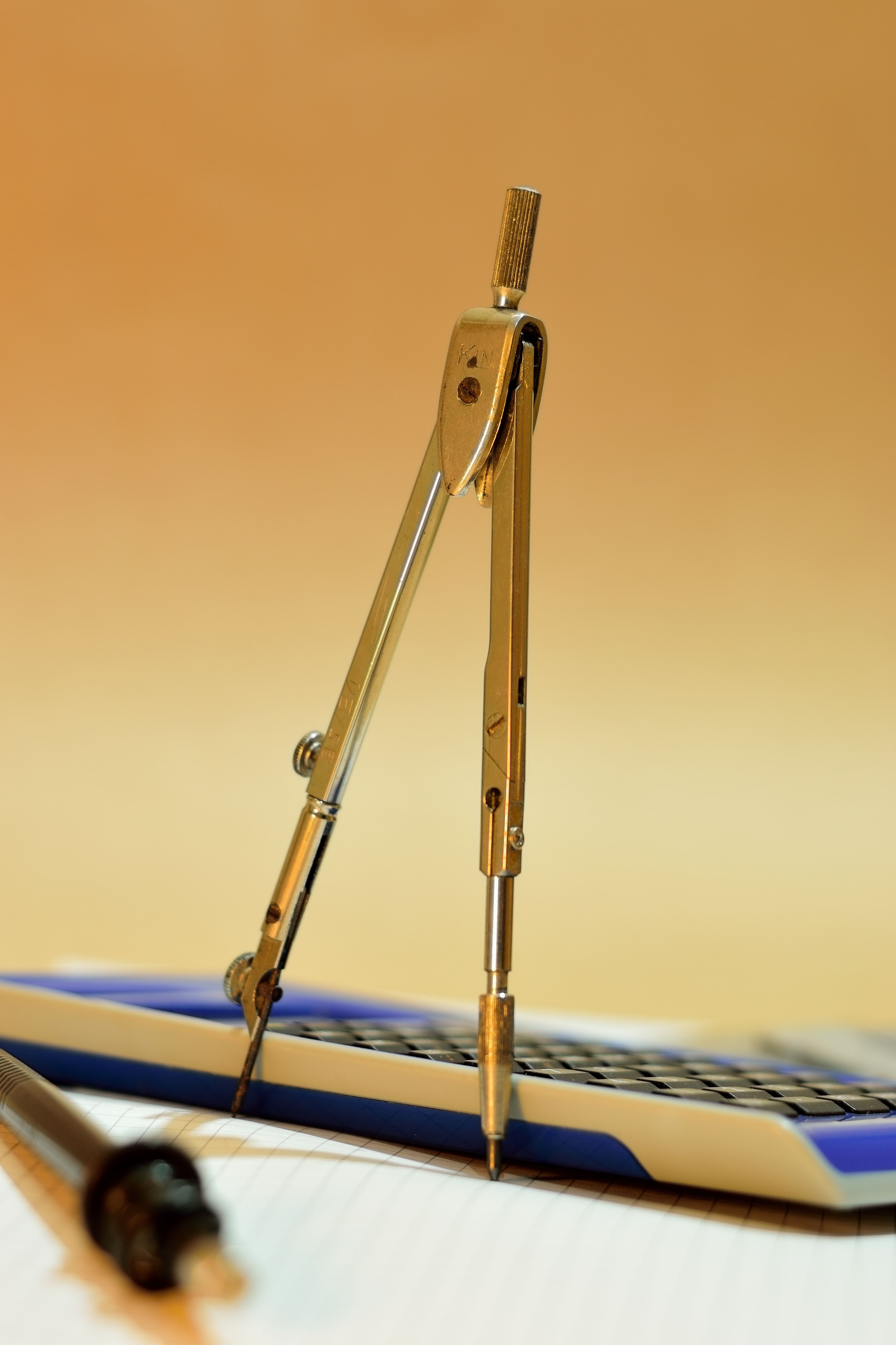 Close-up of a drafting compass on a lined notebook, with a pen and calculator.