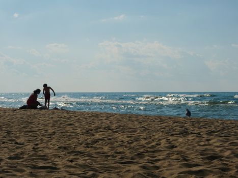 A summer day with people relaxing on a sandy beach by the ocean under a blue sky.