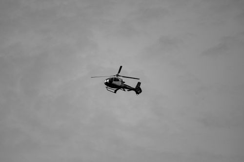 Free A black and white photo of a helicopter flying against a textured sky background, showcasing aviation dynamics. Stock Photo
