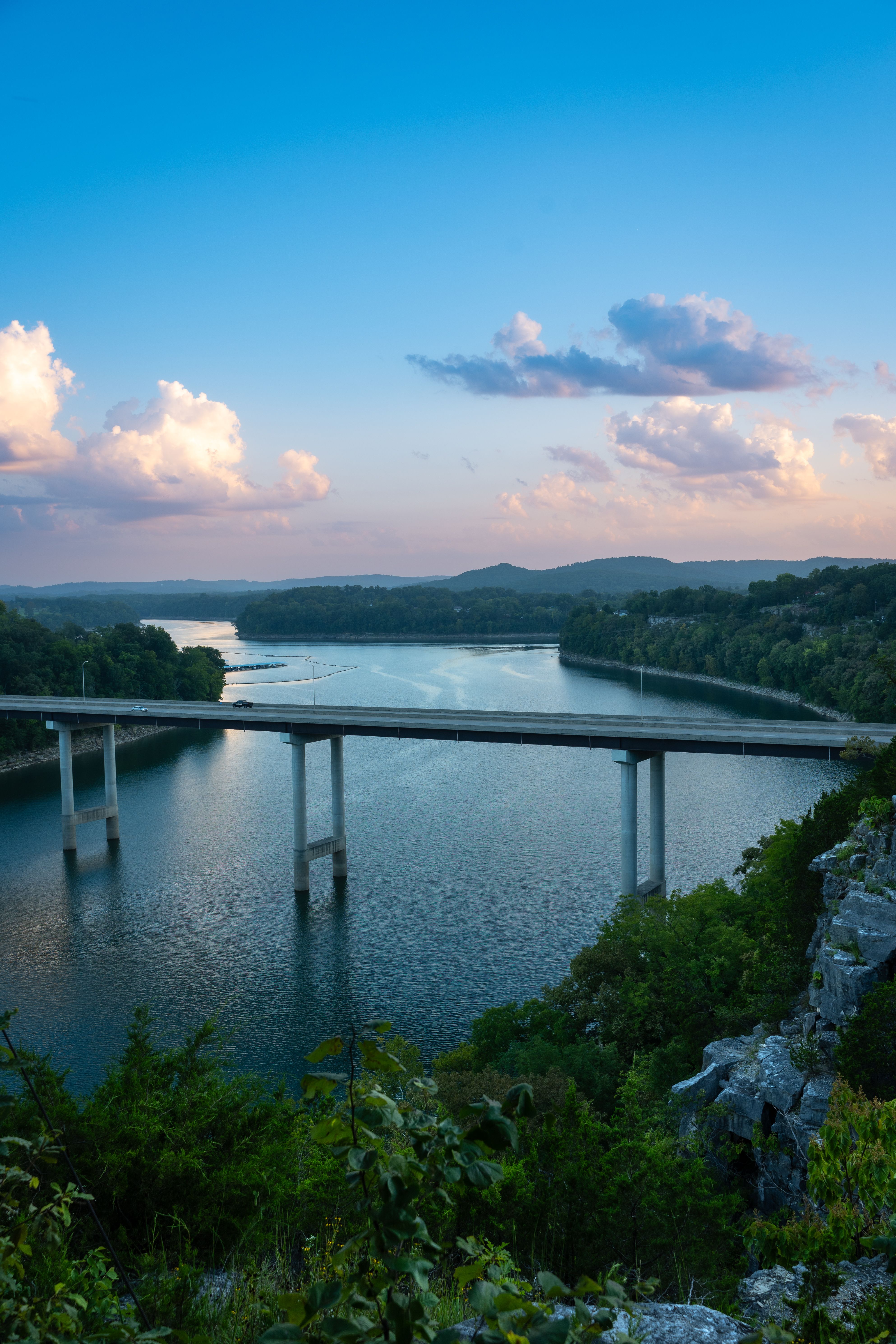 A breathtaking view of a modern bridge crossing a peaceful river surrounded by lush greenery at dusk.