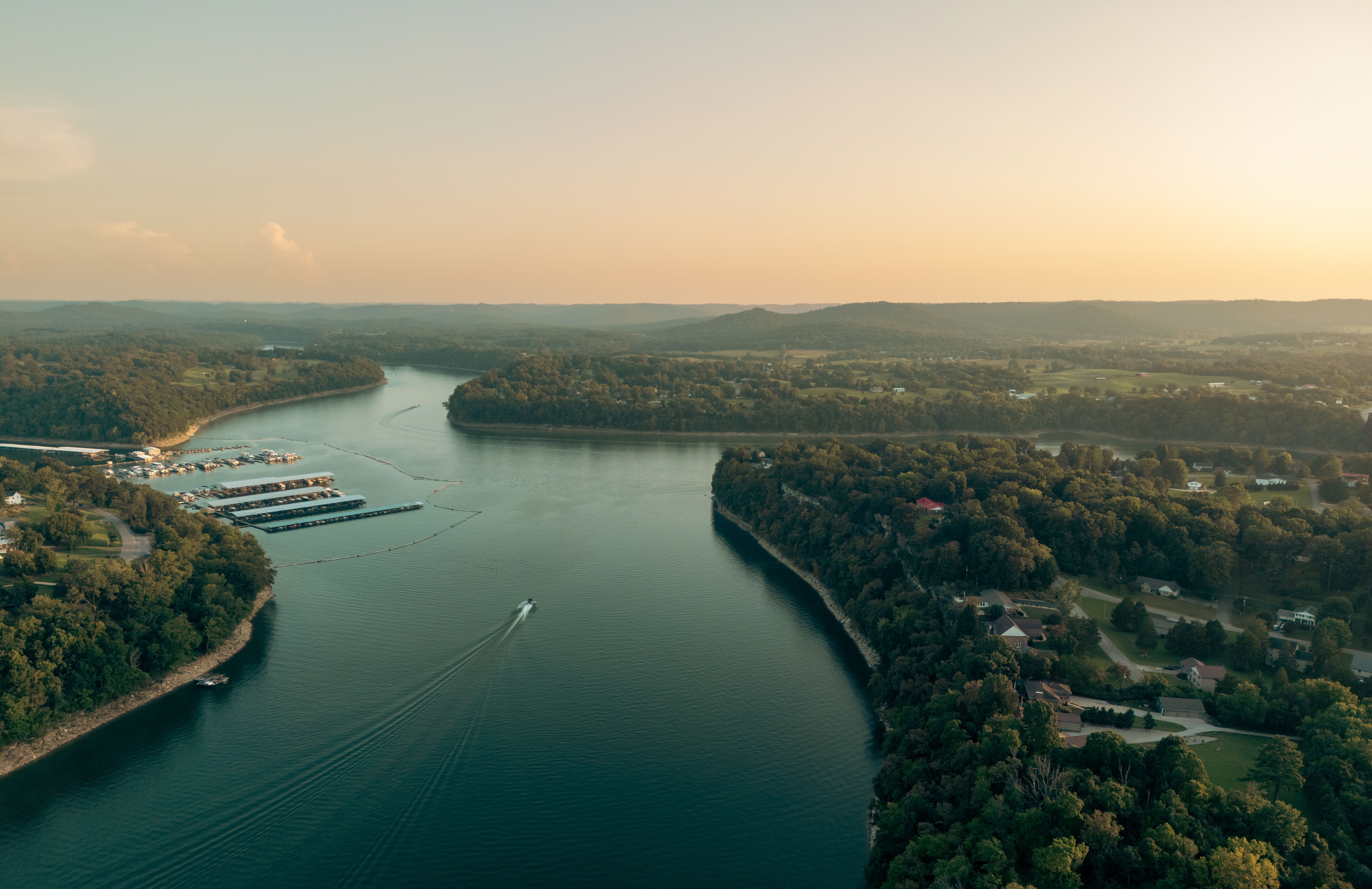 Aerial view of a wide river surrounded by lush forest at sunset
