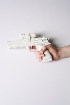 A minimalist photo of a white plastic toy gun held by a hand against a white background.