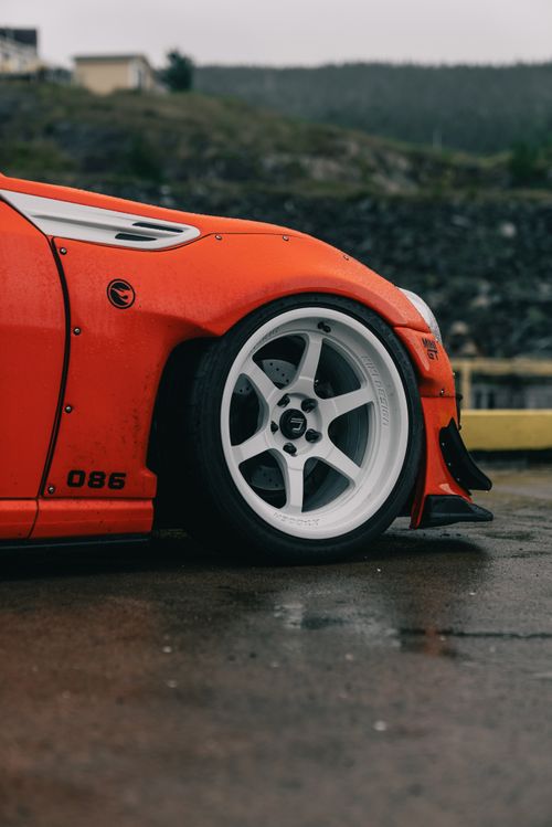 Free Close-up view of a red sports car's front wheel, showcasing sleek design and wet pavement. Stock Photo