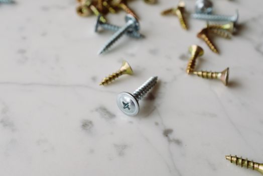 Close-up image of various steel screws scattered on a marble surface showcasing detail and texture.