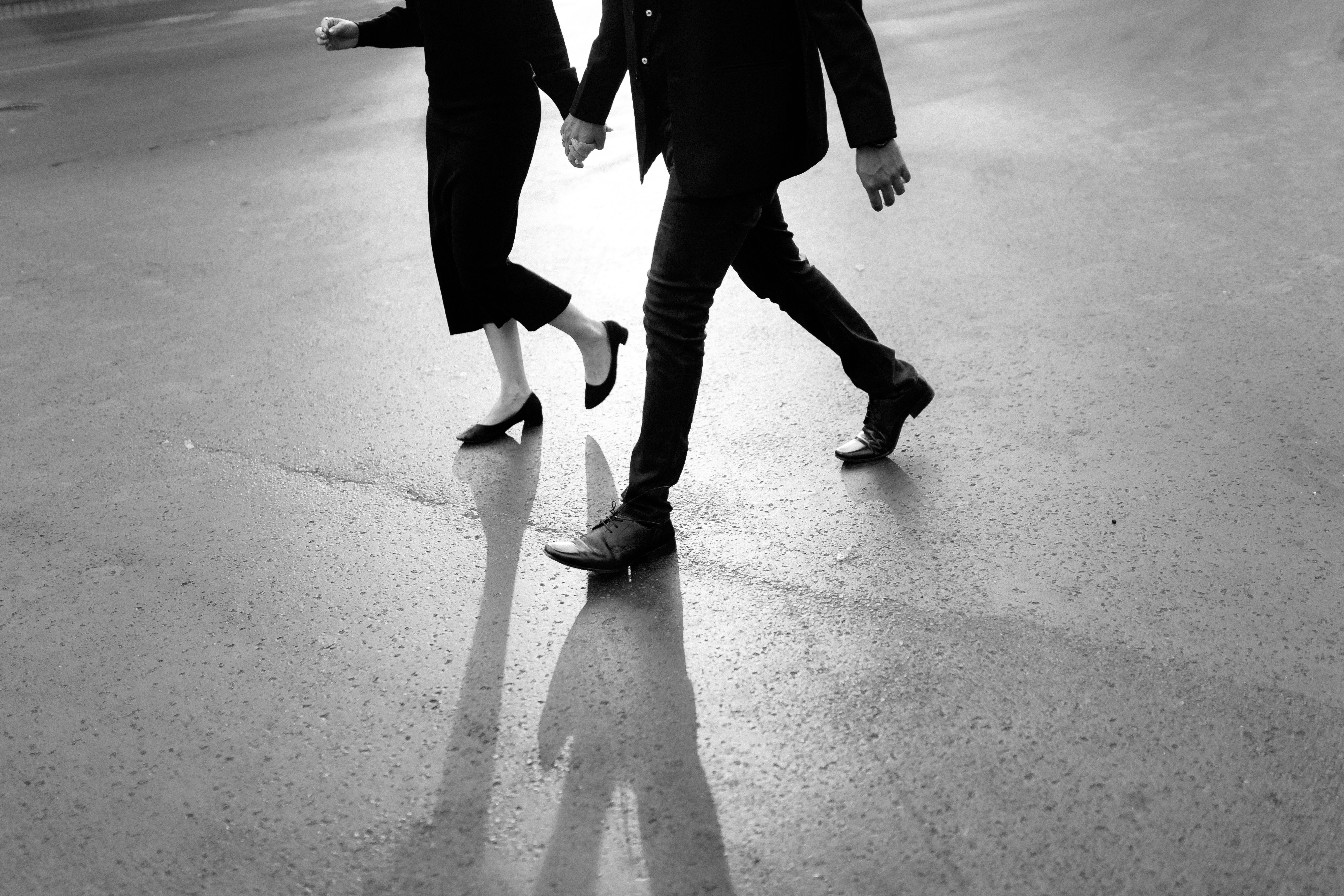 A couple holding hands while walking on a city street, captured in black and white.