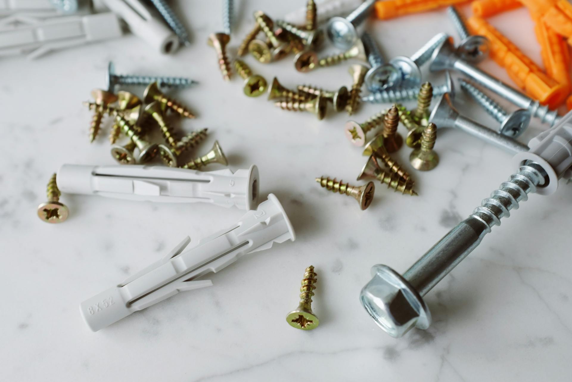 Closeup view of set of various multicolored plastic dowels and metal screws placed on white marble table in modern workshop