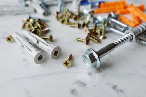 Closeup view of various multicolored plastic dowels with metal screws of different sizes placed on white marble table in modern workshop