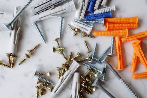 Set of various multicolored plastic dowels with metal screws of different sizes placed on white marble table in modern workshop