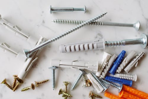 Set of various multicolored plastic dowels with metal screws of different sizes placed on white marble table in modern workshop