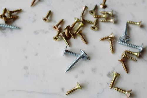 Set of various metal screws of different sizes placed on white marble table in modern workshop