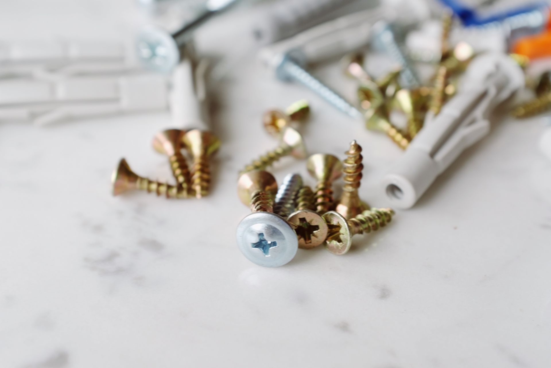 Close-up view of a variety of screws and wall plugs scattered on a marble surface for DIY projects.