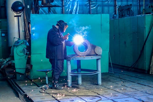 Professional worker welding metal details in factory