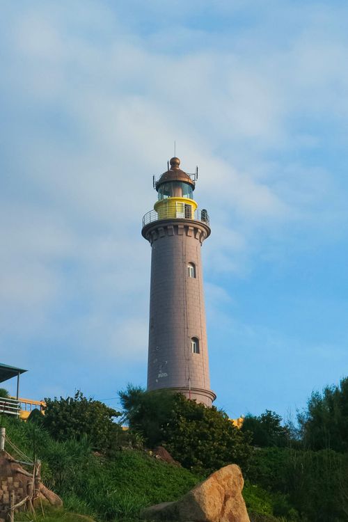 Free Elevated view of a historic lighthouse amidst lush greenery in Phu Yen, Vietnam under a blue sky. Stock Photo
