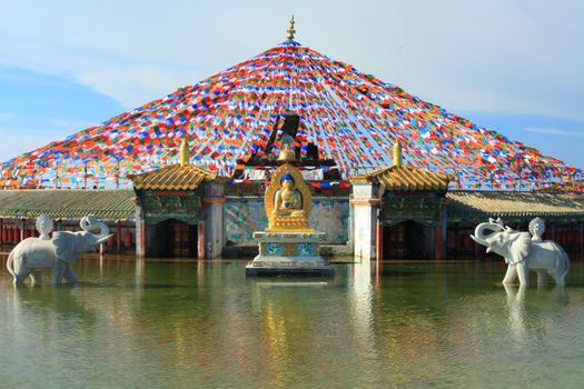 Vibrant Buddhist temple with prayer flags and elephant statues reflected in water.