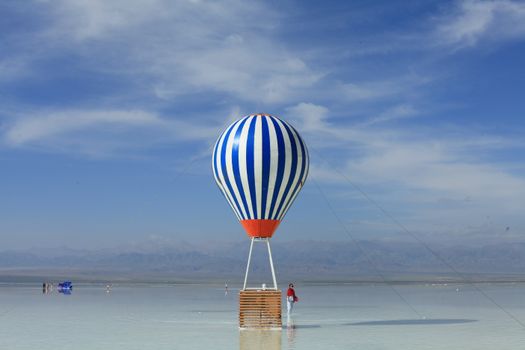Blue and white hot air balloon reflecting on a tranquil salt lake. Clear sky.
