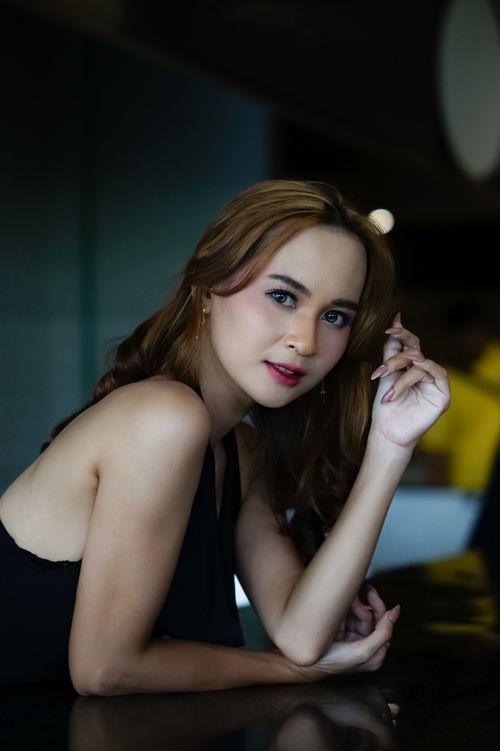 Free A sophisticated woman in a black dress posing elegantly indoors with a soft focus background. Stock Photo
