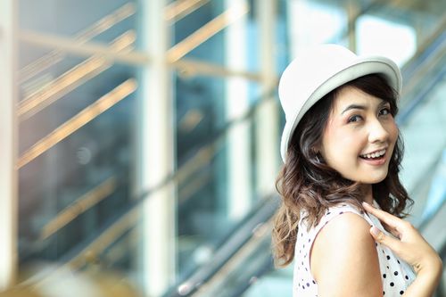 Free A cheerful young woman in a white hat smiles brightly by an escalator indoors. Stock Photo