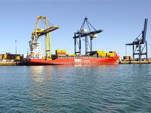 Free A vibrant scene of a cargo ship in Cádiz harbor, flanked by towering cranes and containers. Stock Photo
