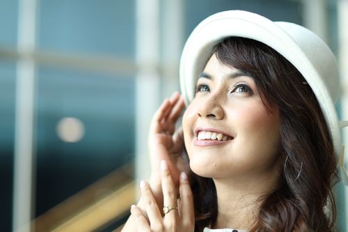 Free Portrait of a smiling woman in a white hat looking upwards indoors with natural light. Stock Photo