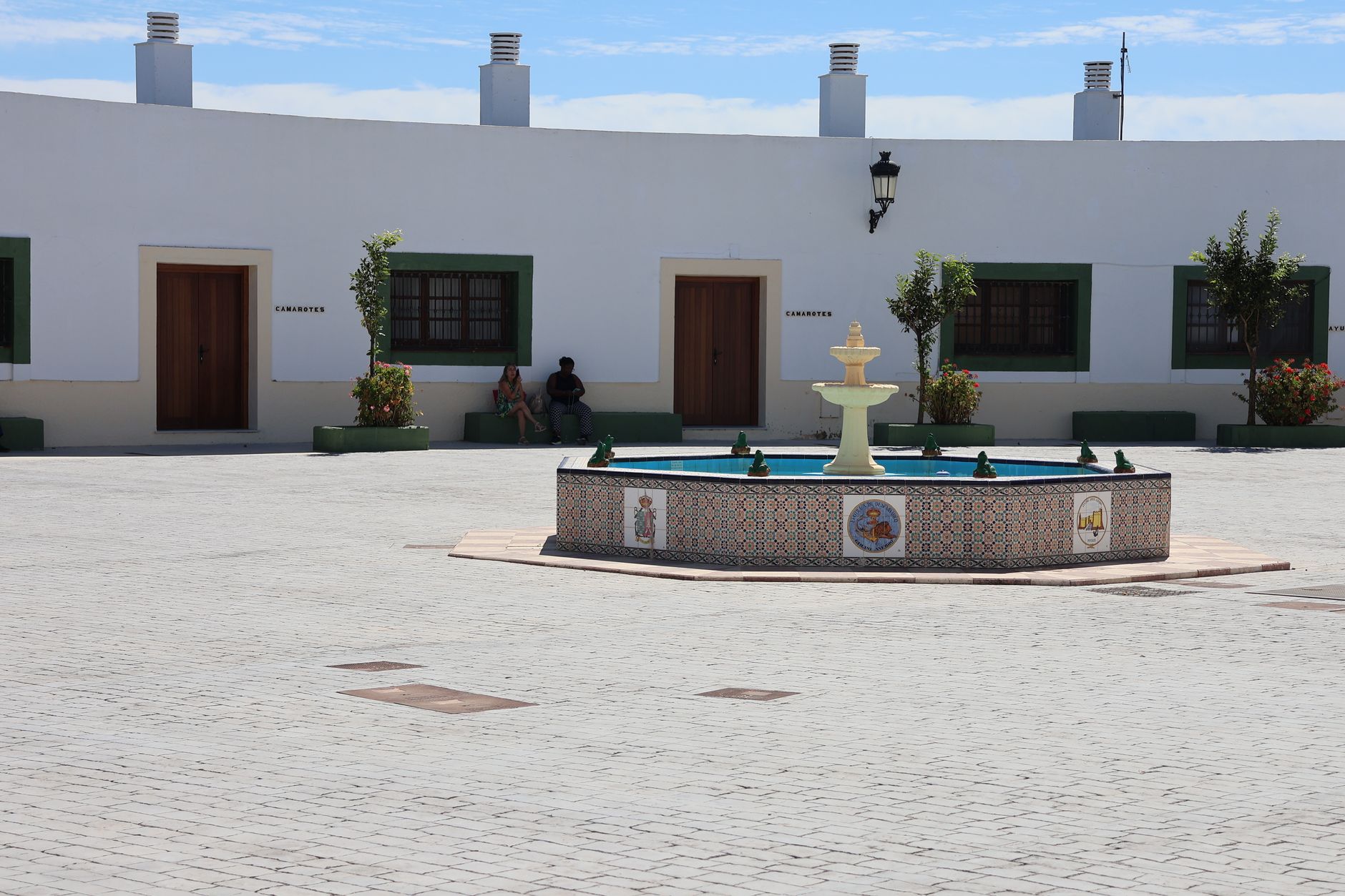 Sunny courtyard in Cádiz featuring a tile-adorned fountain and traditional architecture.