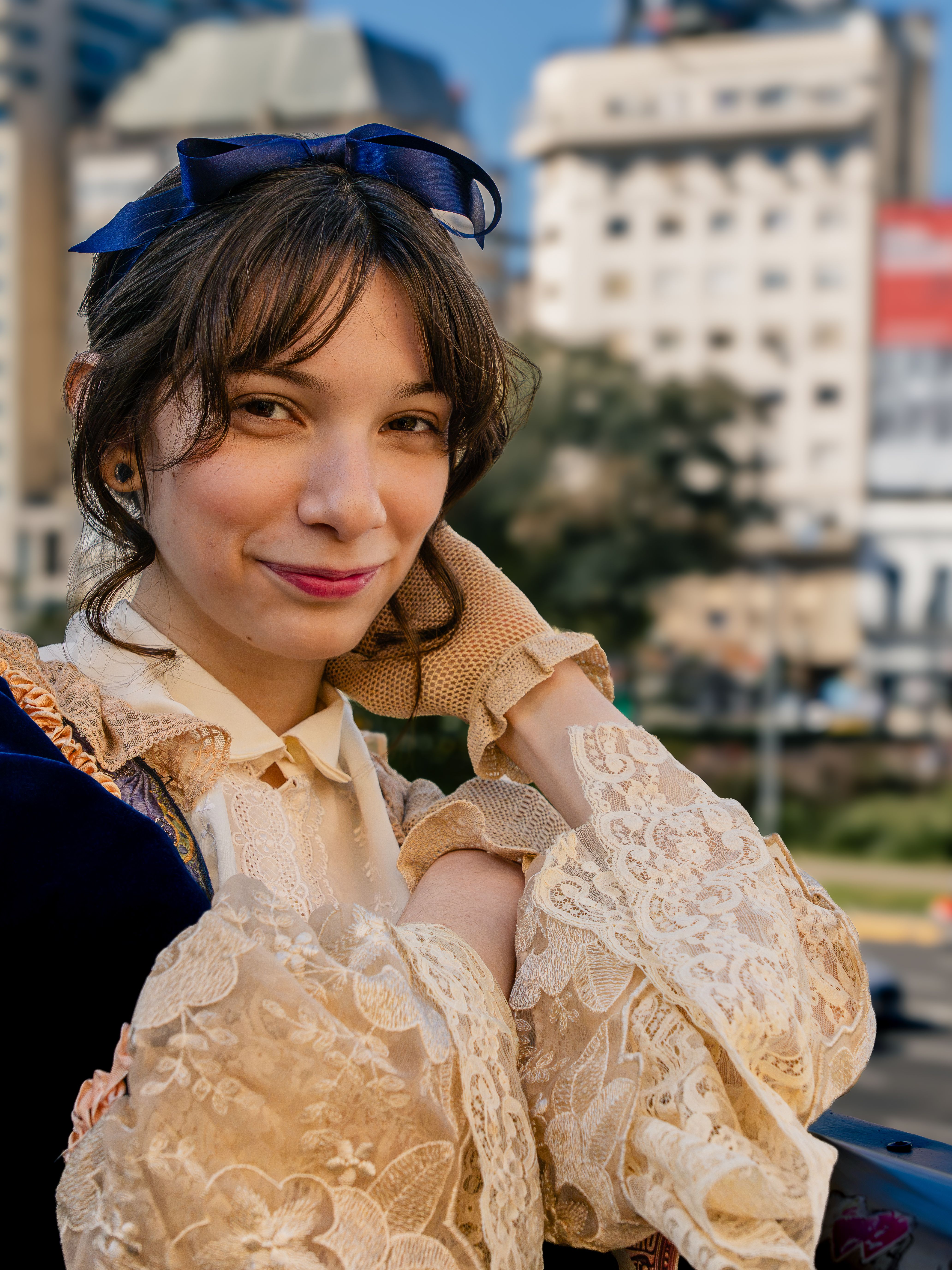 A woman in a Victorian-style outfit poses with historic Buenos Aires in the background.