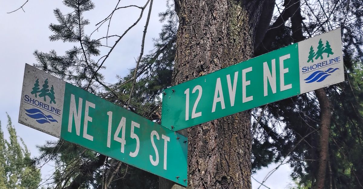 Intersection of NE 145 St and 12 Ave NE street signs in Shoreline, surrounded by trees.
