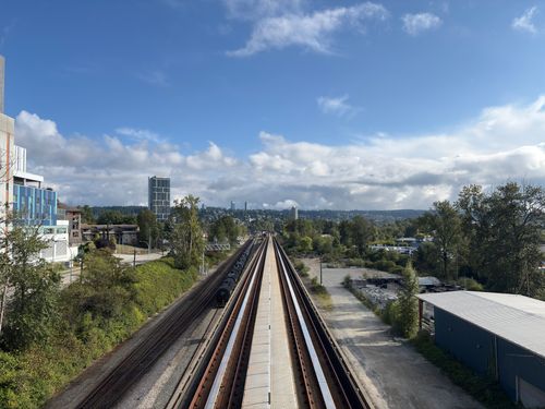 Free Expansive view of train tracks leading through the lush landscape of Vancouver, British Columbia under a bright sky. Stock Photo