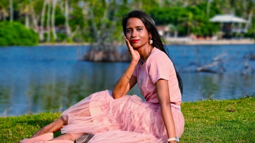 Free Elegant woman in pink attire posing gracefully by a serene lakeside. Stock Photo