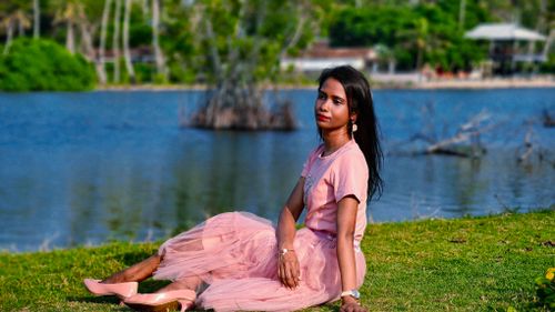 Free An elegant woman in a pink outfit sitting peacefully by the lakeside, enjoying a serene outdoor ambiance. Stock Photo