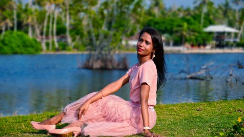 Free A serene portrait of a woman in a pink outfit sitting by a peaceful lake under daylight. Stock Photo