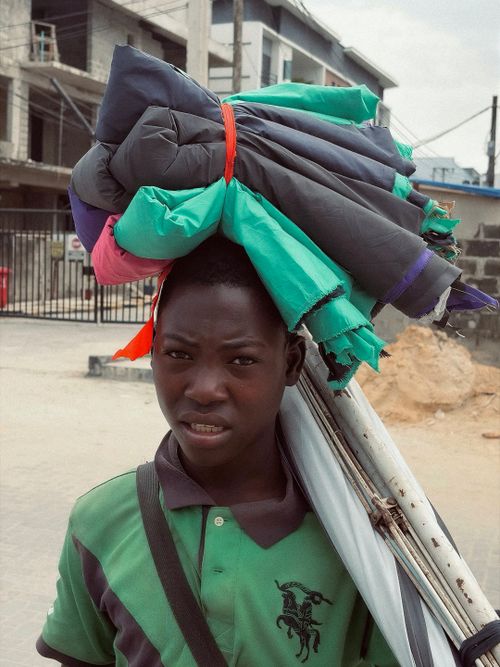Free Young boy carries clothes on head on a Nigerian street, showcasing daily life. Stock Photo
