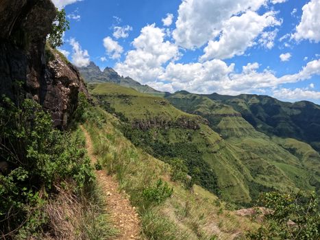 Experience the breathtaking views of rugged cliffs and lush green hills in Drakensberg, South Africa.